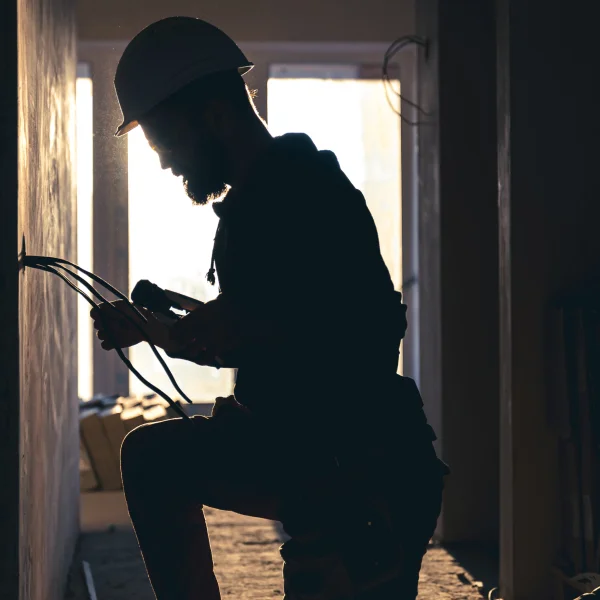 Un homme en casque de sécurité travaille sur un mur, se concentrant sur des travaux d'électricité résidentielle.
